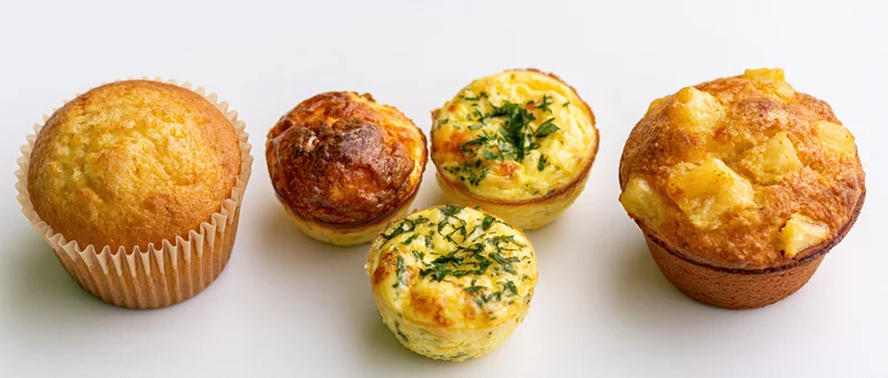 Five assorted muffins arranged in a row on a white background