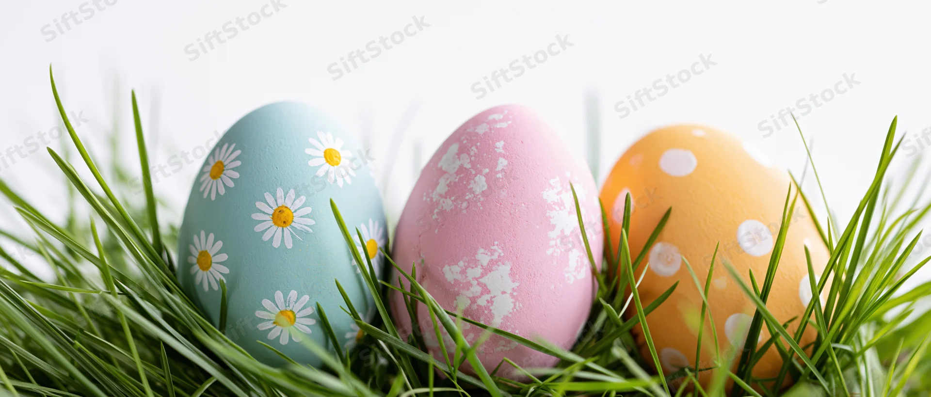 Three painted easter eggs with floral and polka dot patterns nestled in green grass