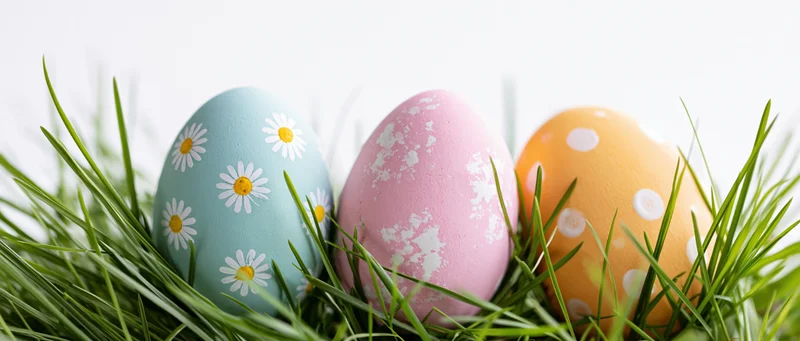 Three painted easter eggs with floral and polka dot patterns nestled in green grass