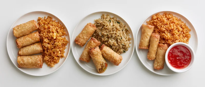Three white plates with springrolls and fried rice arranged side by side on a white surface