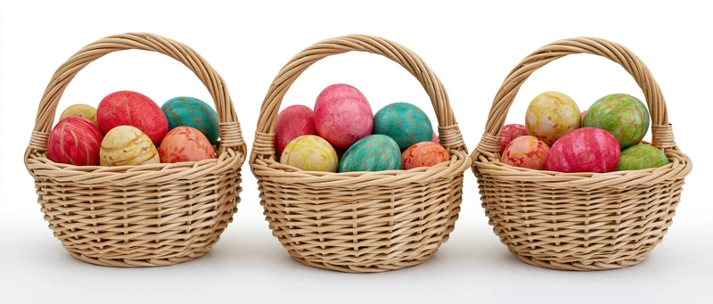 Three wicker baskets filled with hand-painted colorful eggs arranged in a row on a white background
