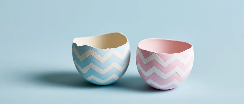 Two cracked easter egg shell halves with chevron pattern on a light blue surface