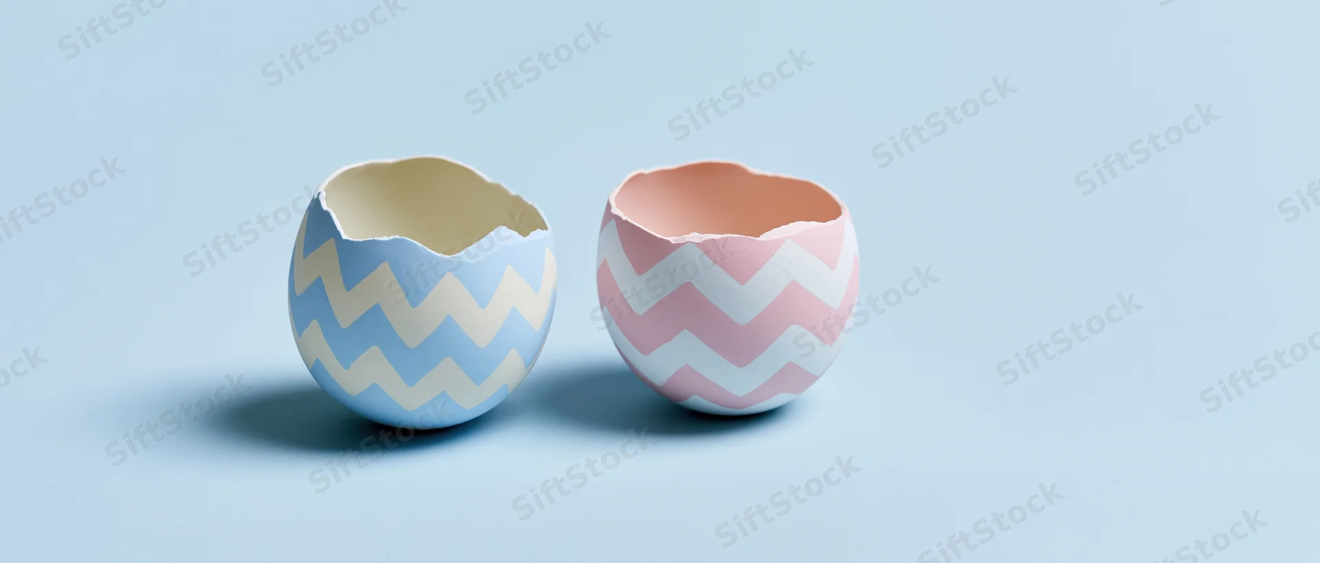 Two cracked easter egg shells with zigzag patterns sitting open on a light blue surface