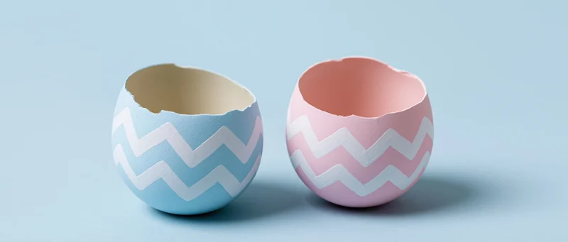 Two cracked easter egg shells with zigzag patterns sitting open on a light blue surface