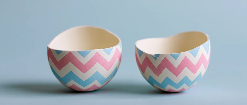 Two decorated easter egg shell halves split apart and facing up on a light blue surface
