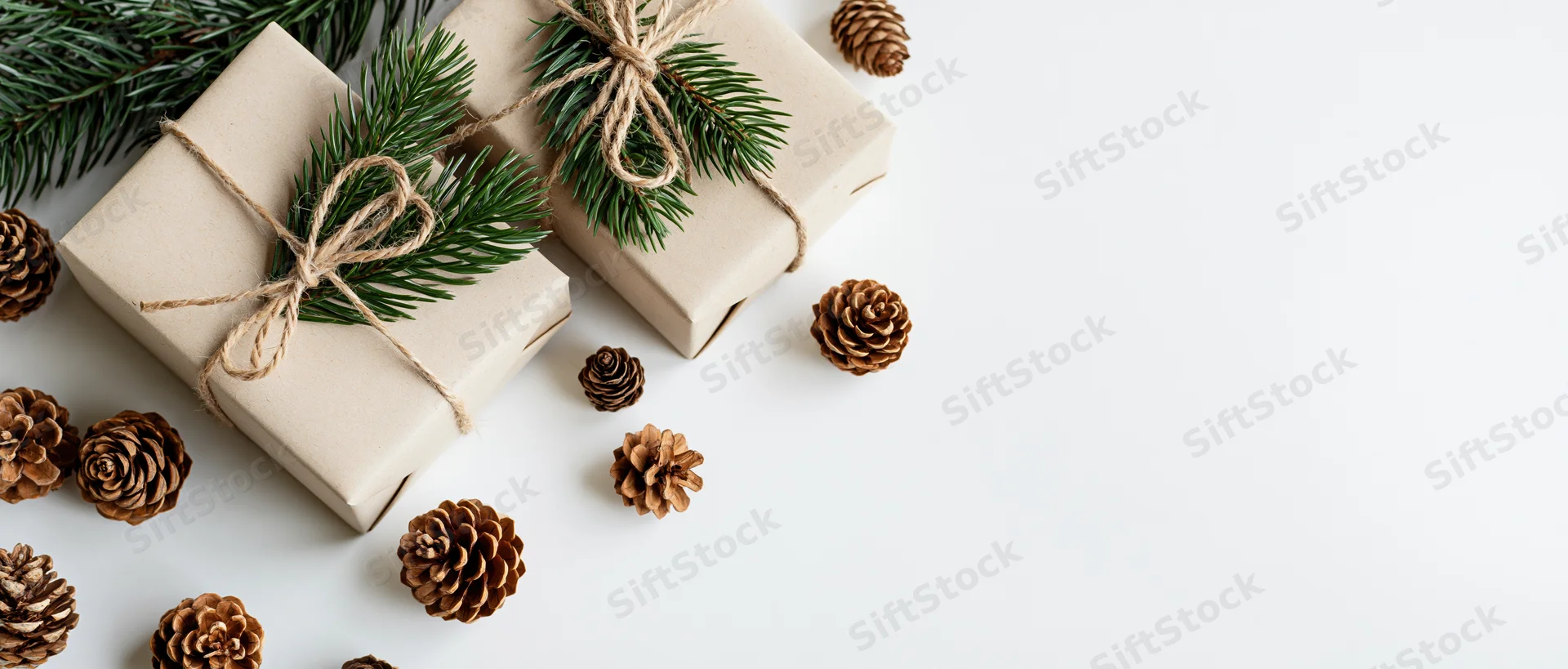 Two kraft paper gift boxes tied with twine and decorated with pine branches and pinecones on white surface