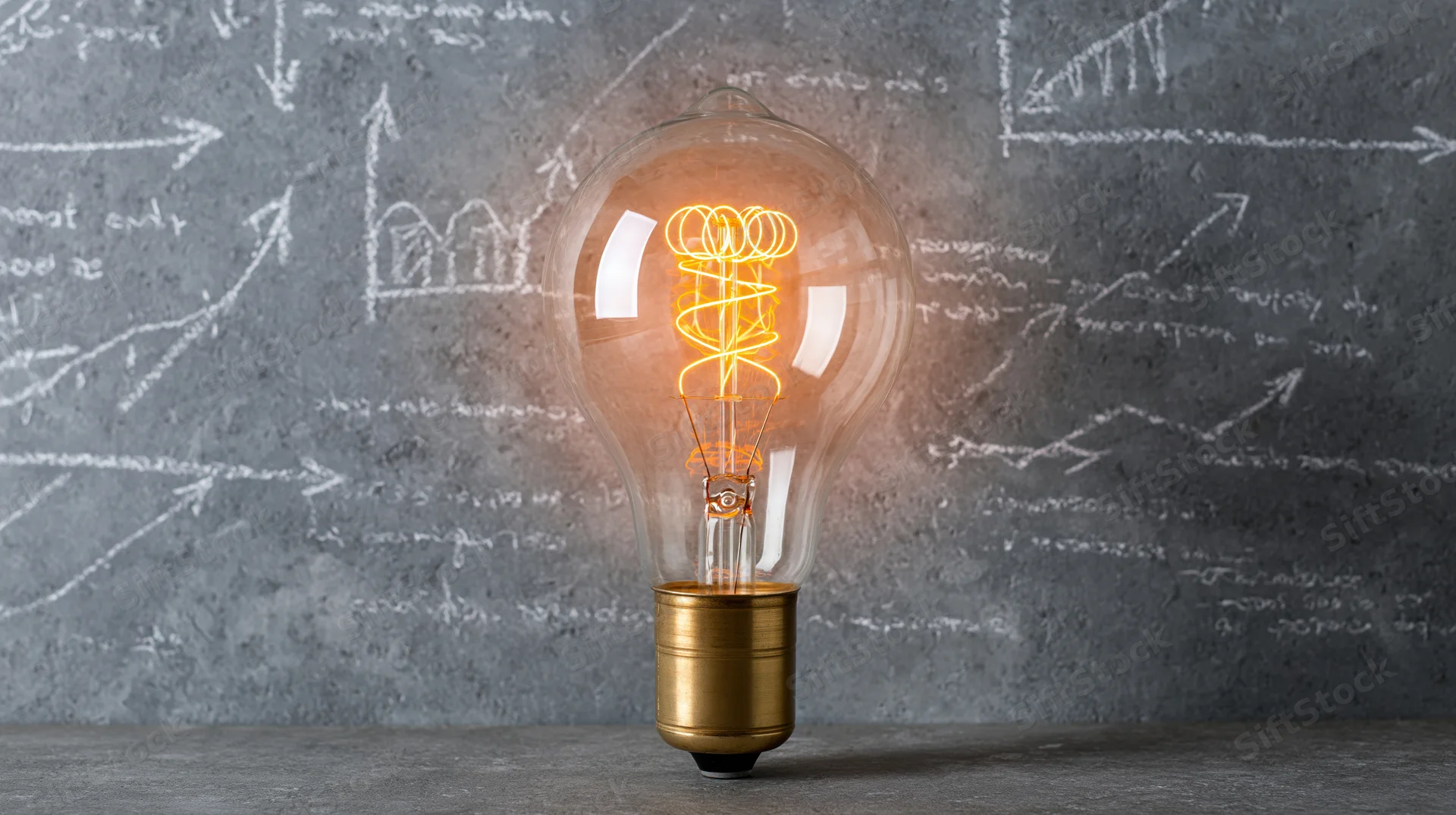 Glowing vintage edison lightbulb on concrete surface with chalk equations and graphs in background