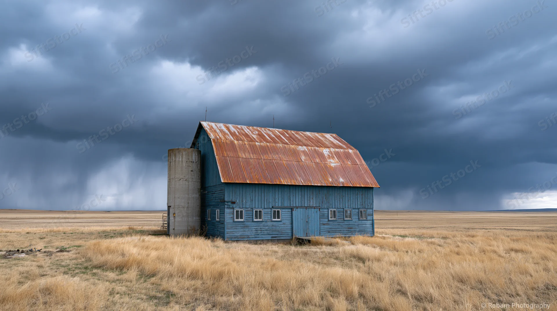 Weathered blue barn with rusted metal roof under stormy sky in open field