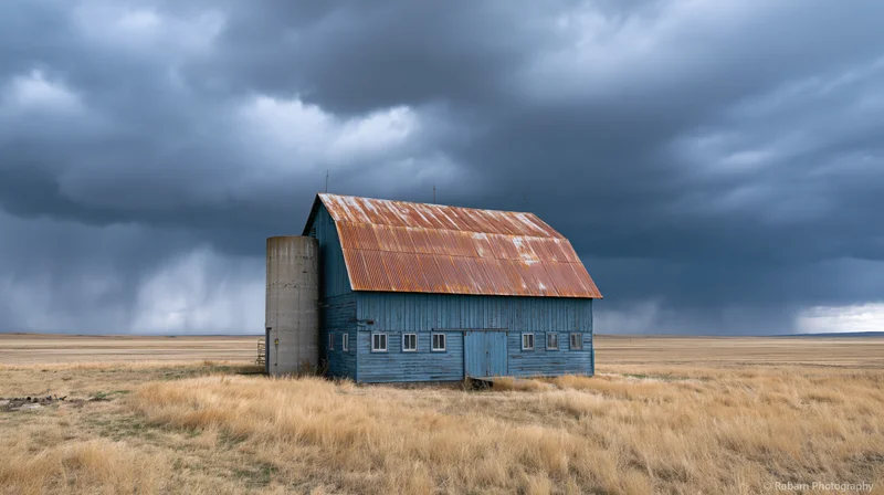 Weathered blue barn with rusted metal roof under stormy sky in open field