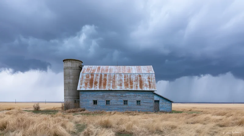 Weathered blue barn with rusted metal roof and silo under stormy sky in open field