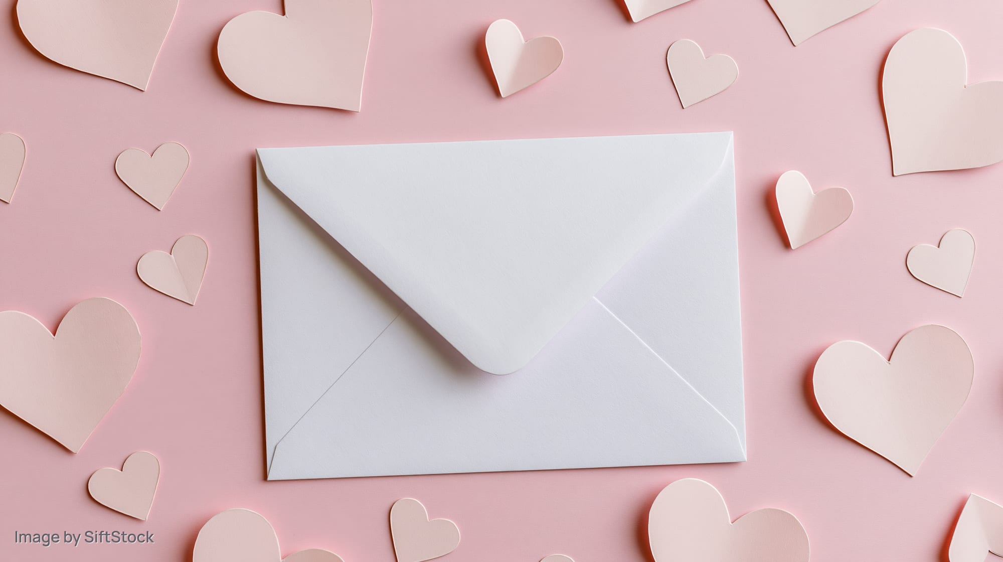 White envelope on pastel pink surface surrounded by paper hearts in flat lay arrangement