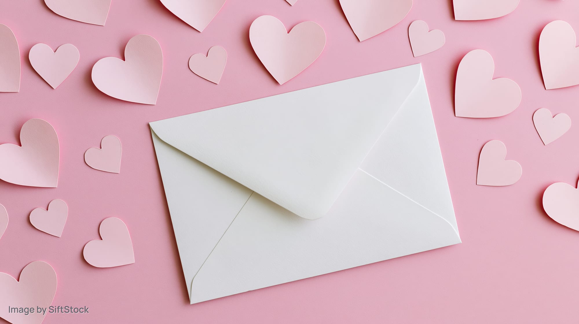 White envelope on a pink surface surrounded by paper hearts