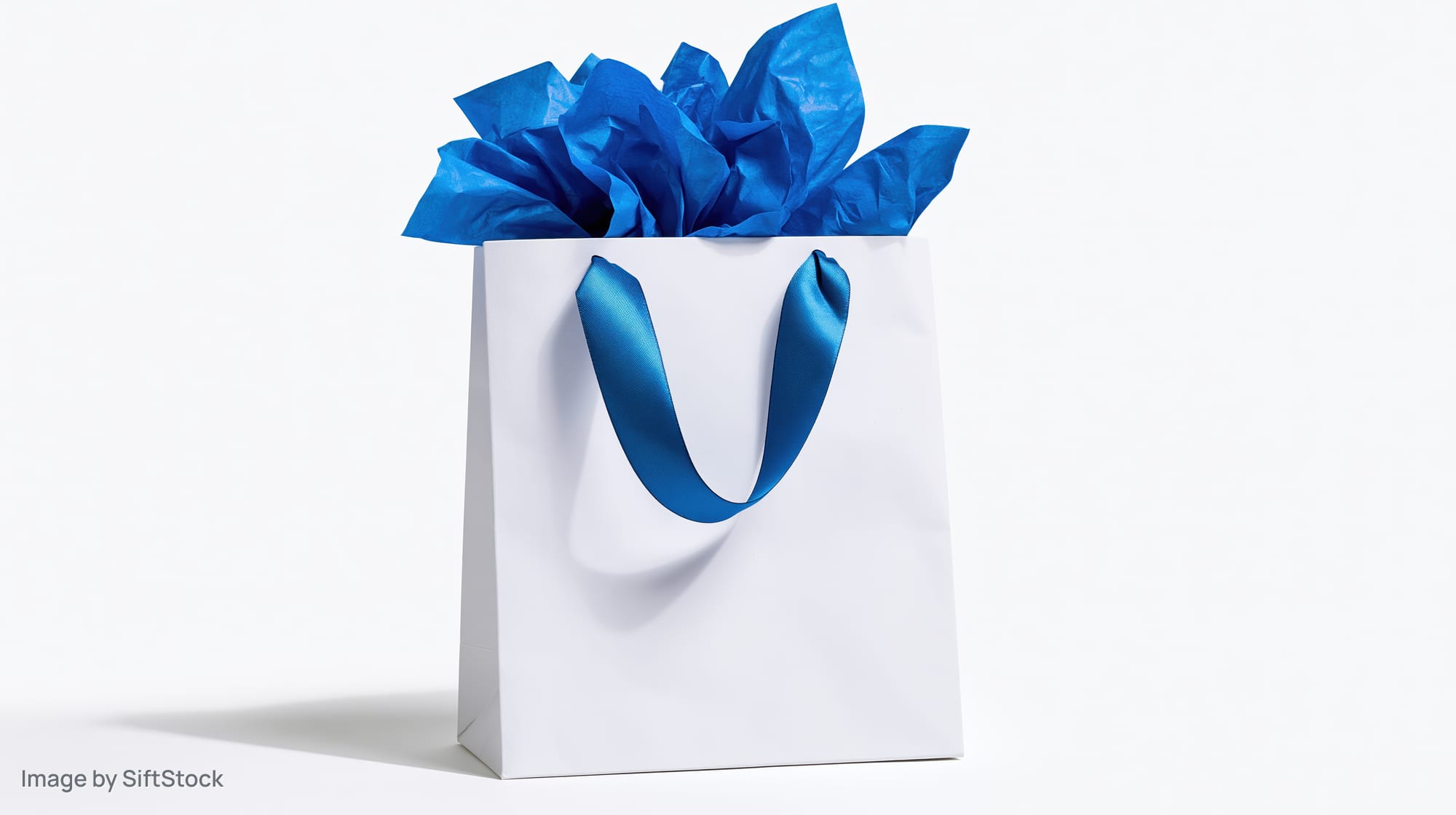 White gift bag with blue satin ribbon handles and crumpled tissue paper on white background