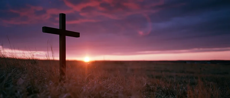 Wooden christian cross standing in a grassy meadow at sunset