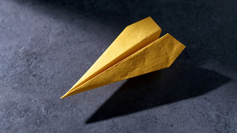 Yellow paper airplane folded and resting on dark textured surface casting sharp shadow