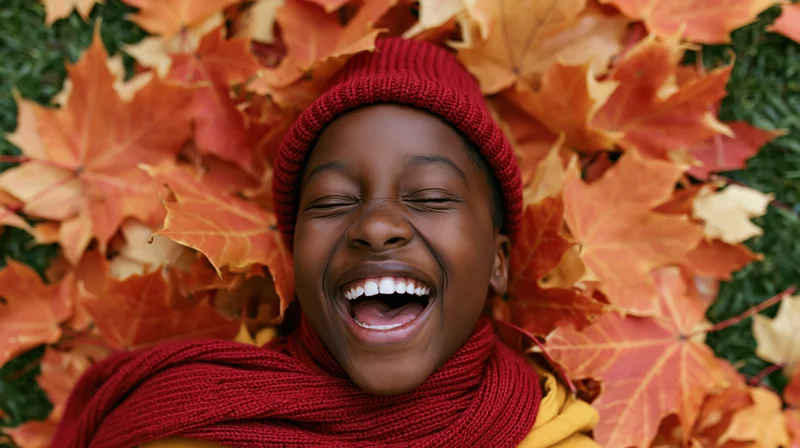 Young black child laughing with eyes closed while lying in a pile of autumn maple leaves
