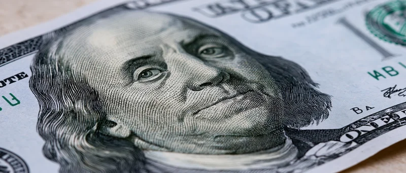 Closeup of a hundred dollar bill showing benjamin franklin's portrait and security details laid flat on a surface