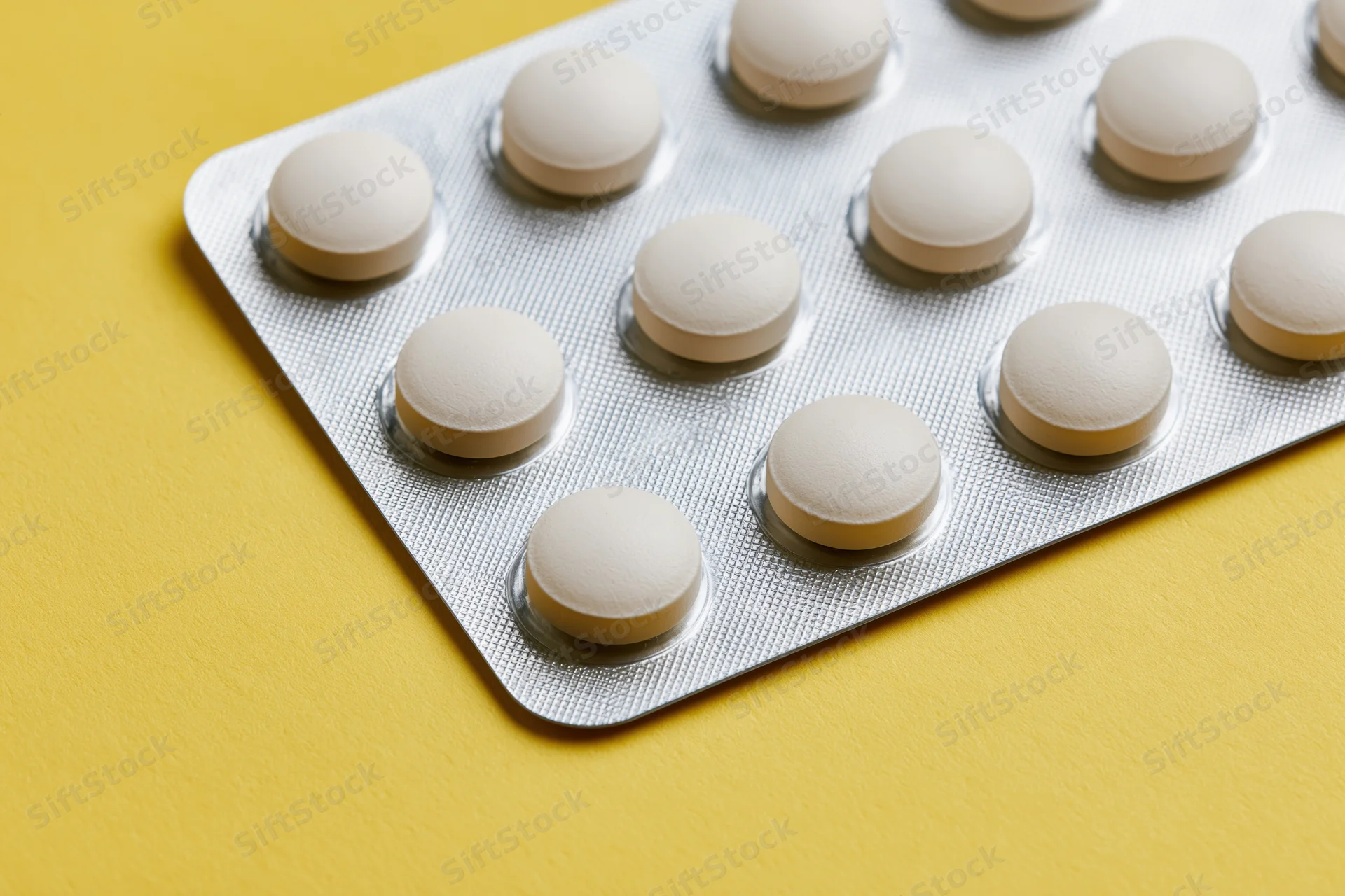 Round white tablets in a blister pack on a yellow surface