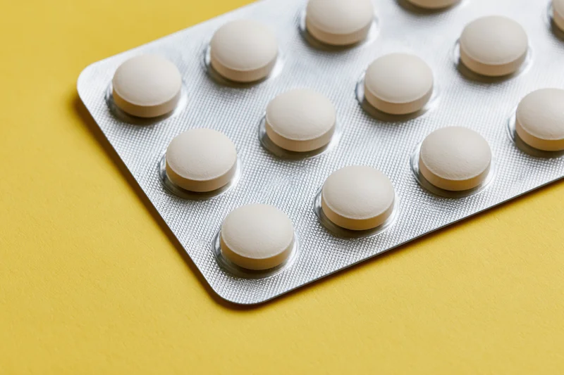 Round white tablets in a blister pack on a yellow surface