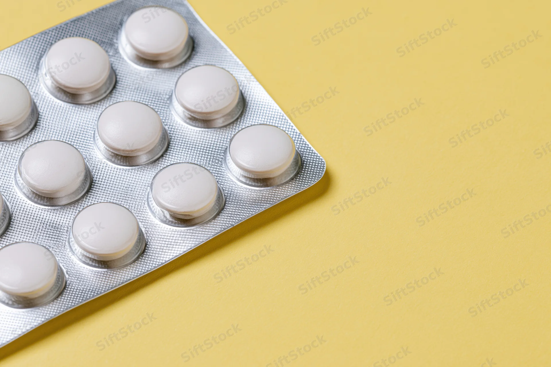 Blister pack of white tablets on yellow surface with copyspace