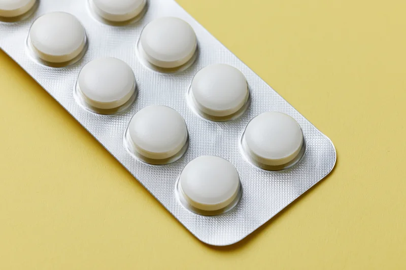Round white tablets in a silver blister pack on a yellow surface