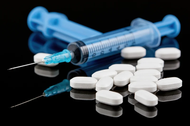 Blue medical syringe with needle and white tablets on reflective black surface