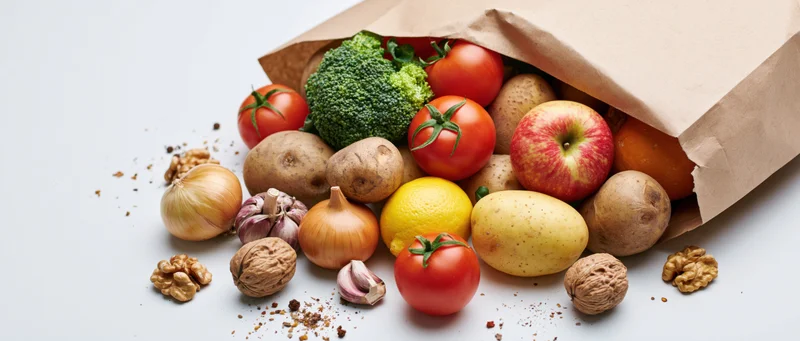 Brown paper grocery bag tipped over spilling fresh produce onto white surface