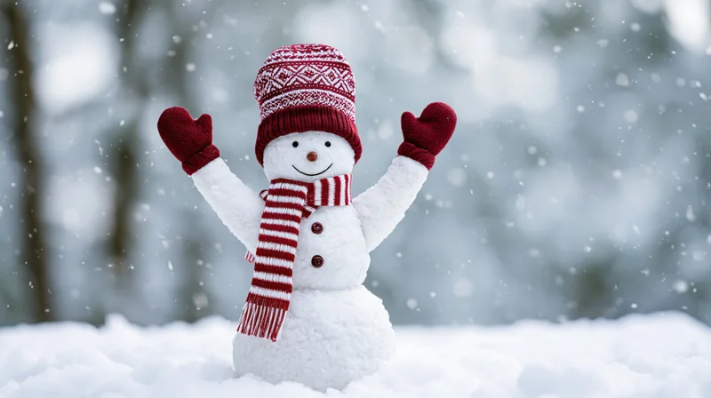Cheerful snowman toy figurine with raised arms in fresh snow wearing red hat scarf and mittens