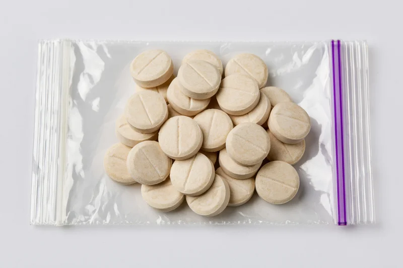 Beige scored tablets in a clear resealable plastic bag on white background