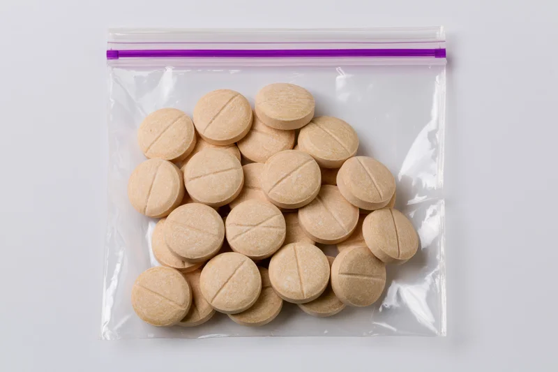Round beige scored tablets in a clear zip-lock bag on white surface