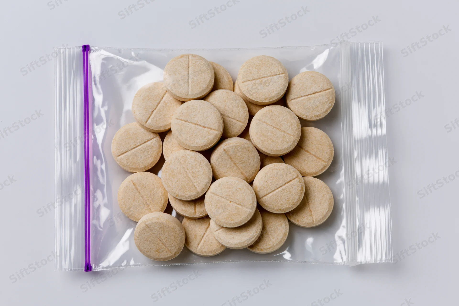 Beige scored tablets in a clear zip-lock bag on white background