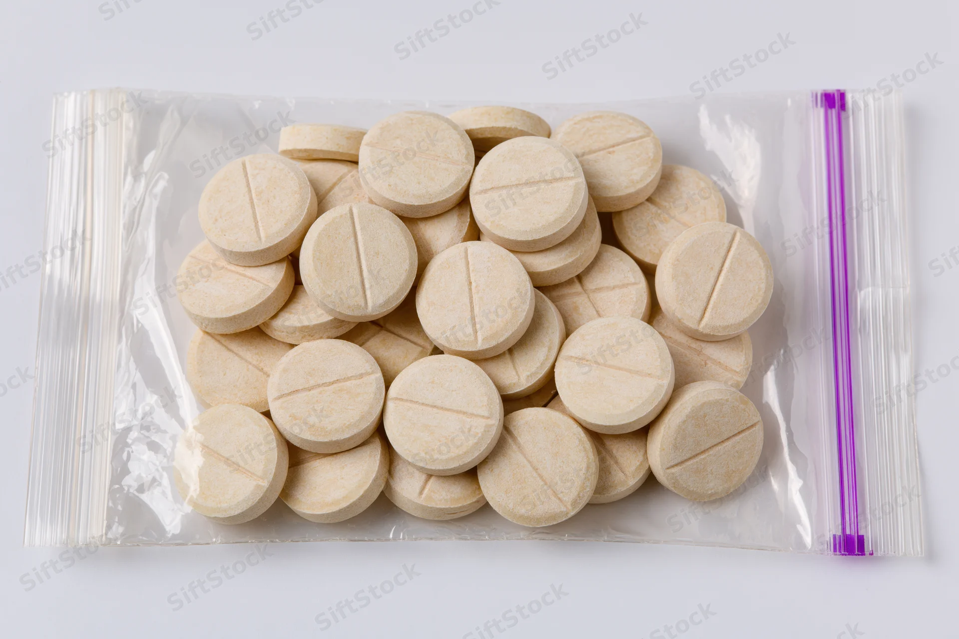 Beige scored tablets in a transparent resealable plastic bag on white background