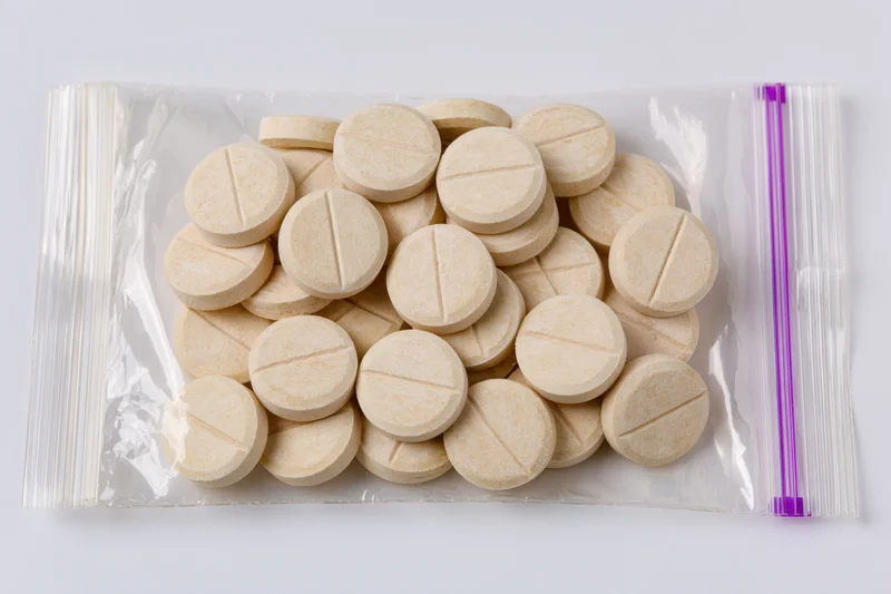 Beige scored tablets in a transparent resealable plastic bag on white background