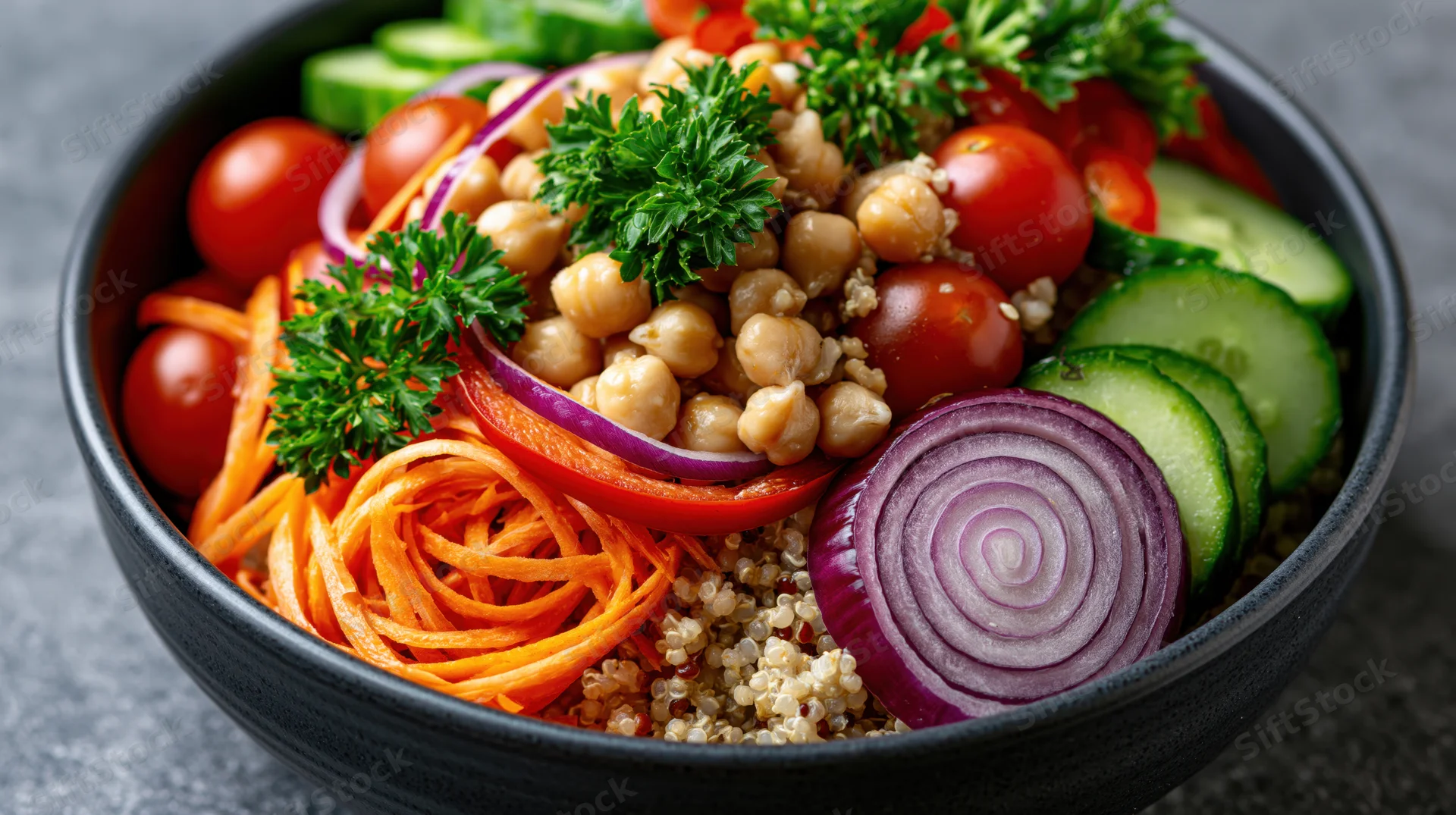 Dark ceramic bowl filled with quinoa salad topped with chickpeas, vegetables and parsley