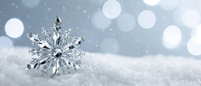 Crystal snowflake ornament resting on snow with bokeh lights in background