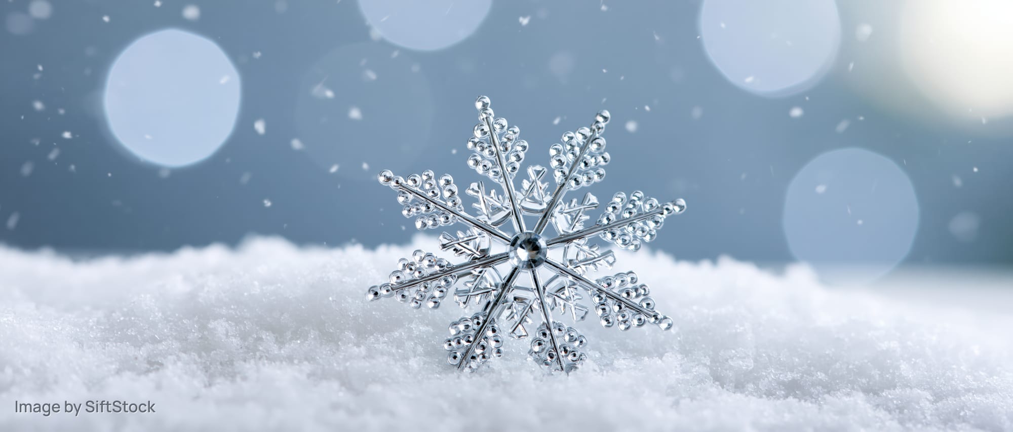 Crystal snowflake ornament resting on soft snow with bokeh lights in background