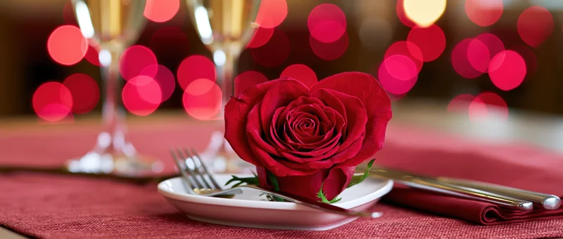 Red rose shaped like a heart resting on a white plate at a romantic dinner table setting