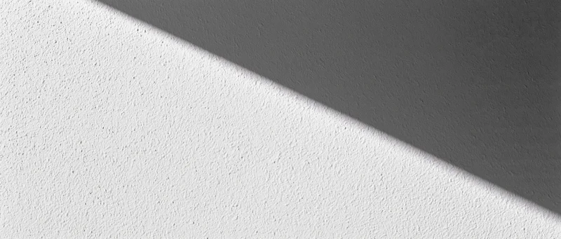 Diagonal shadow across a matte plaster wall in an interior space