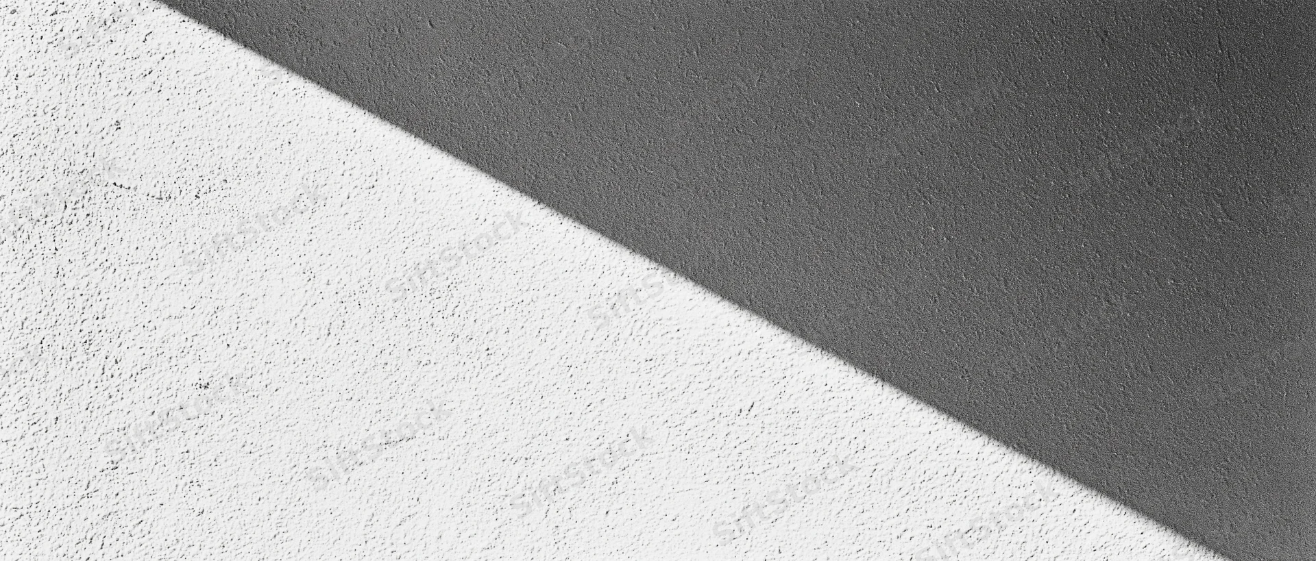 Diagonal shadow across a matte plaster wall dividing light and dark areas