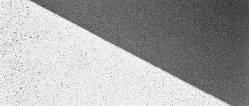 Diagonal shadow across a matte plaster wall dividing light and dark areas