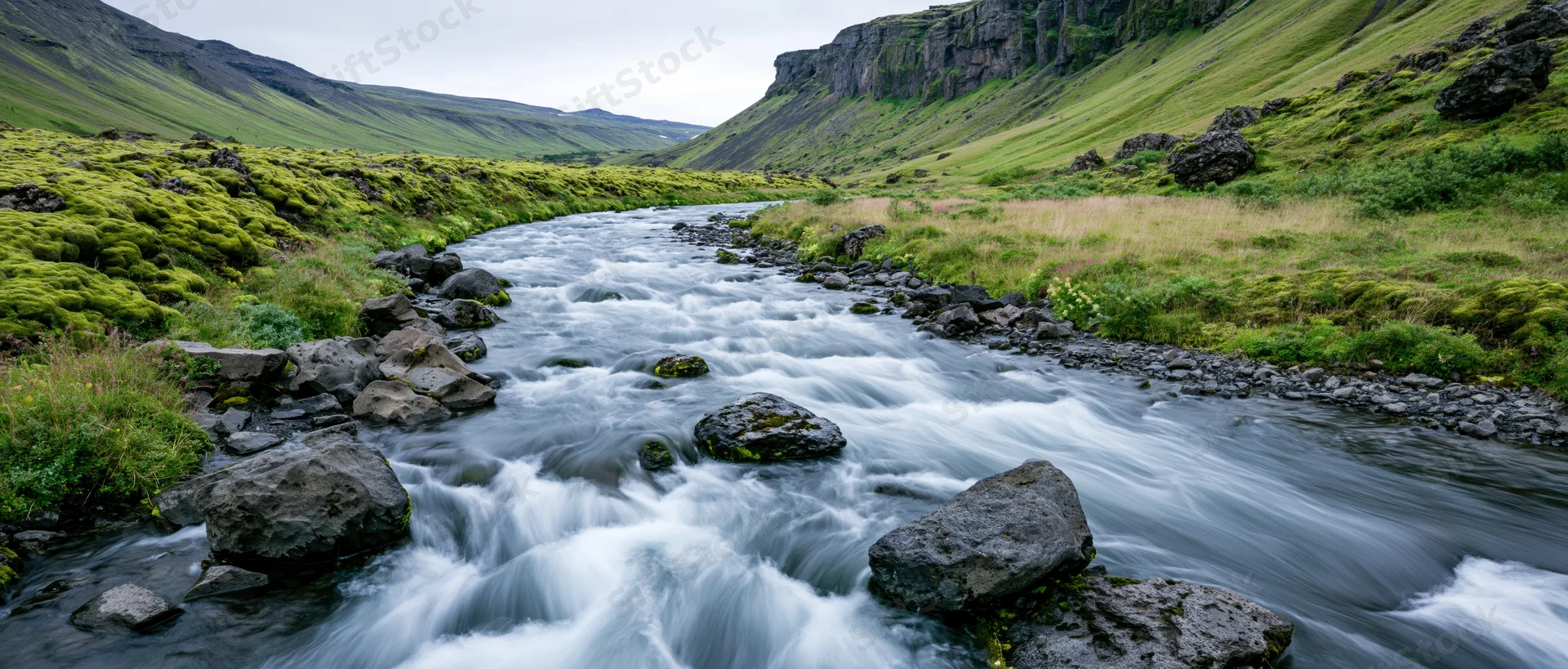 Glacial river rushing over dark volcanic rocks through a green valley
