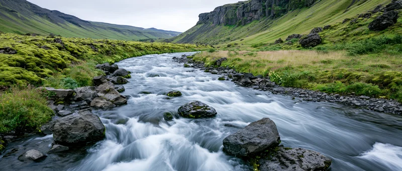 Glacial river rushing over dark volcanic rocks through a green valley