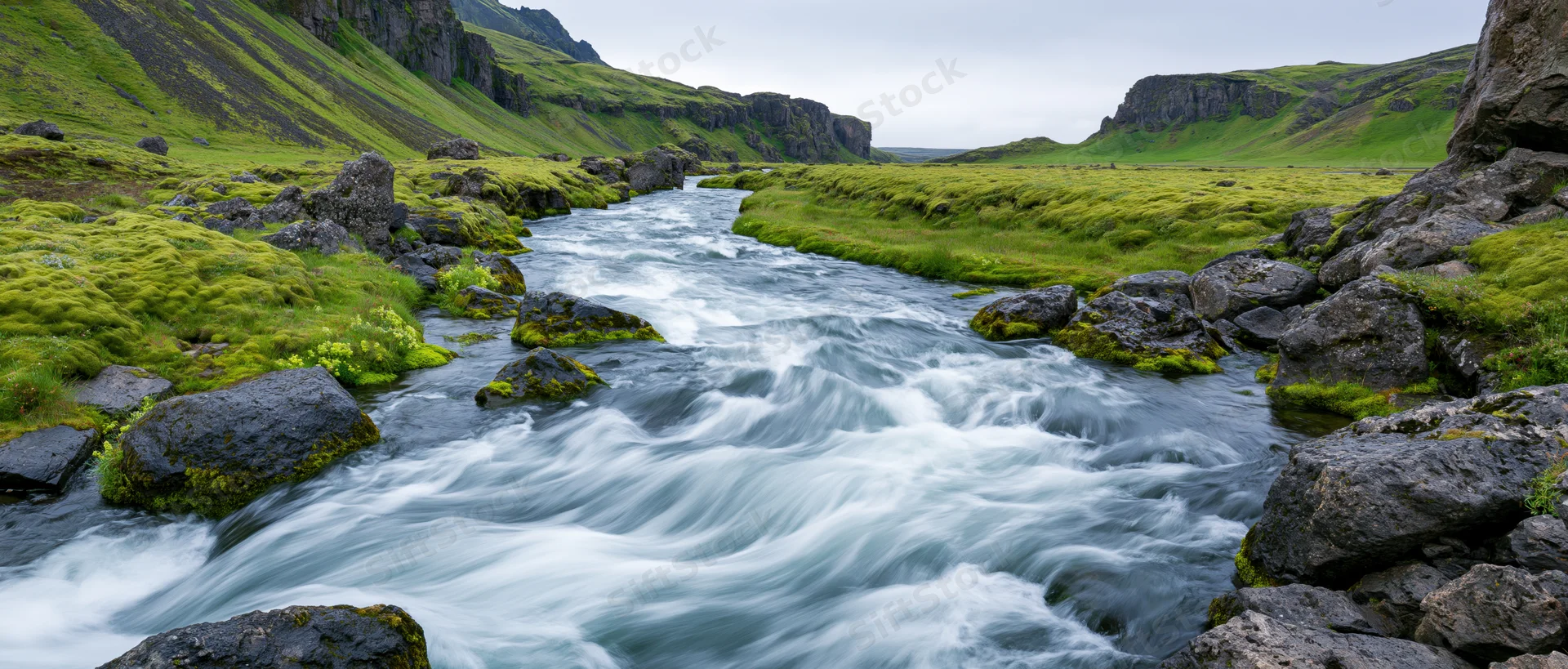 Glacial river rushing over dark volcanic rocks through a green valley