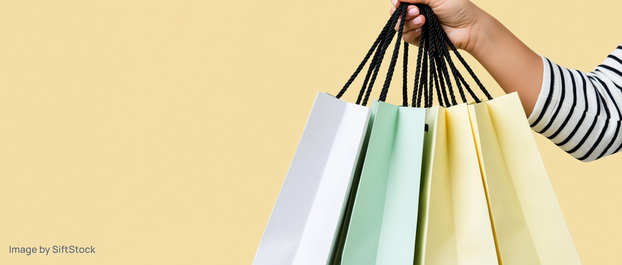 Hand holding multiple paper shopping bags with black rope handles against a yellow background