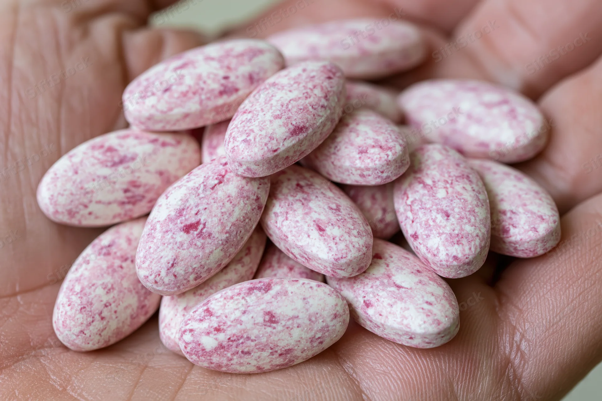 Pink speckled oval tablets piled in an open palm