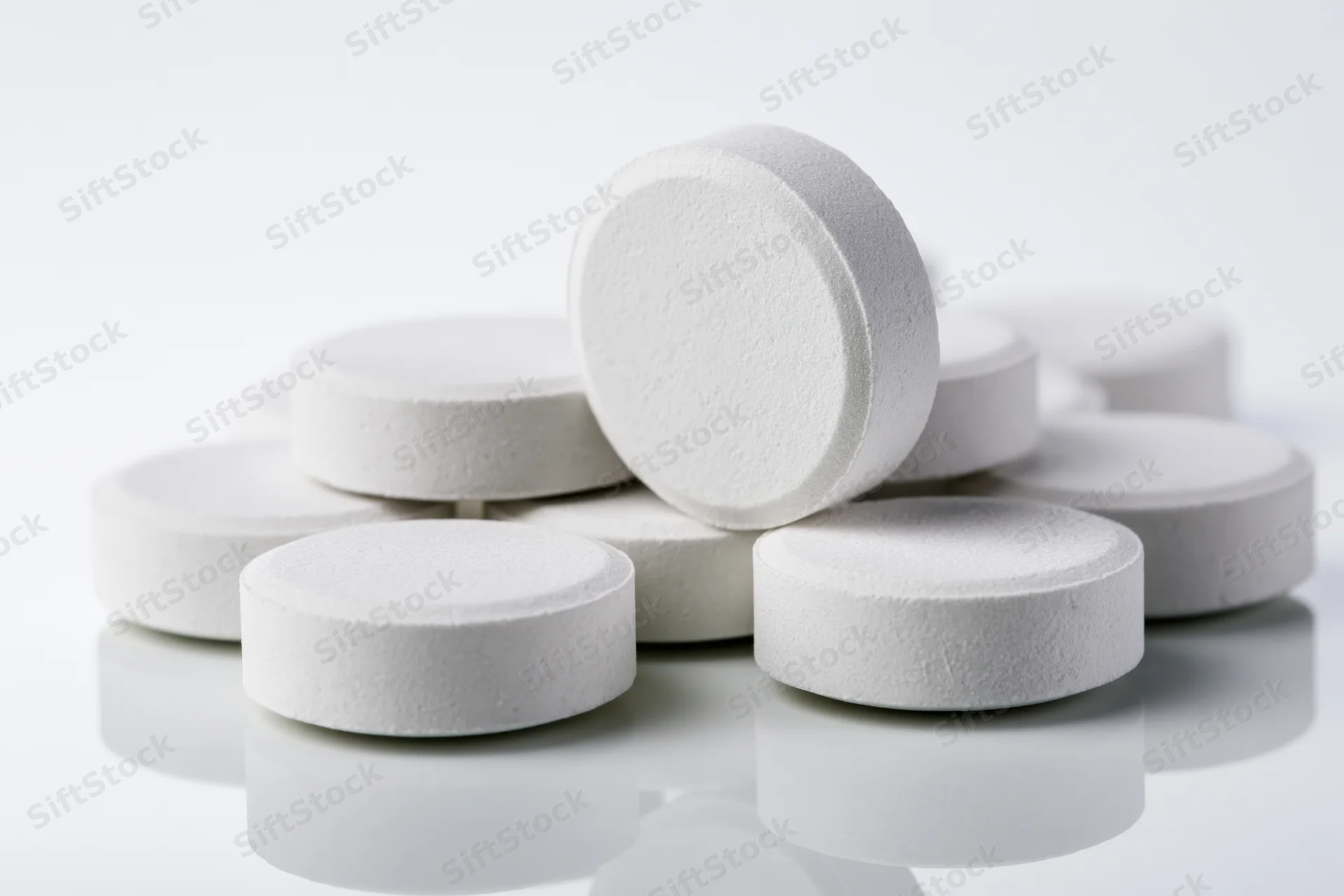 Round white pharmaceutical tablets scattered in a loose cluster on a reflective white surface