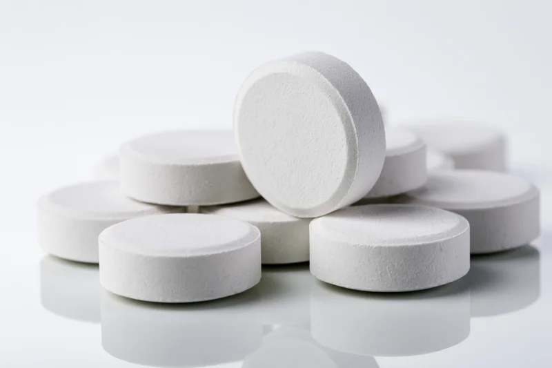Round white pharmaceutical tablets scattered in a loose cluster on a reflective white surface