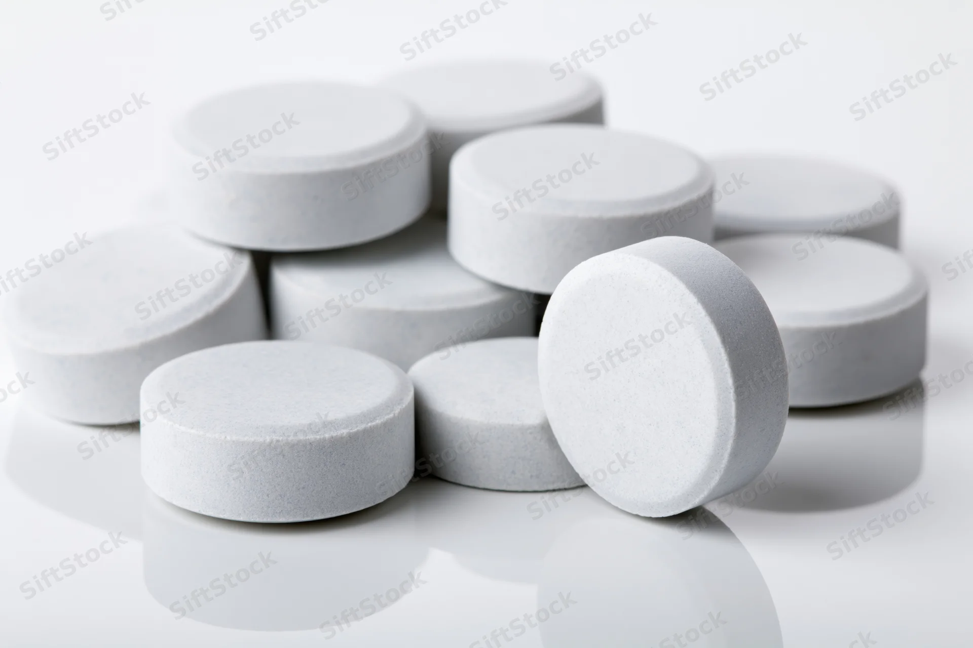 Scattered white pharmaceutical tablets on a reflective white surface