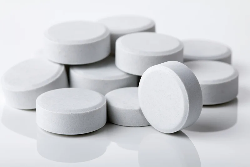 Scattered white pharmaceutical tablets on a reflective white surface