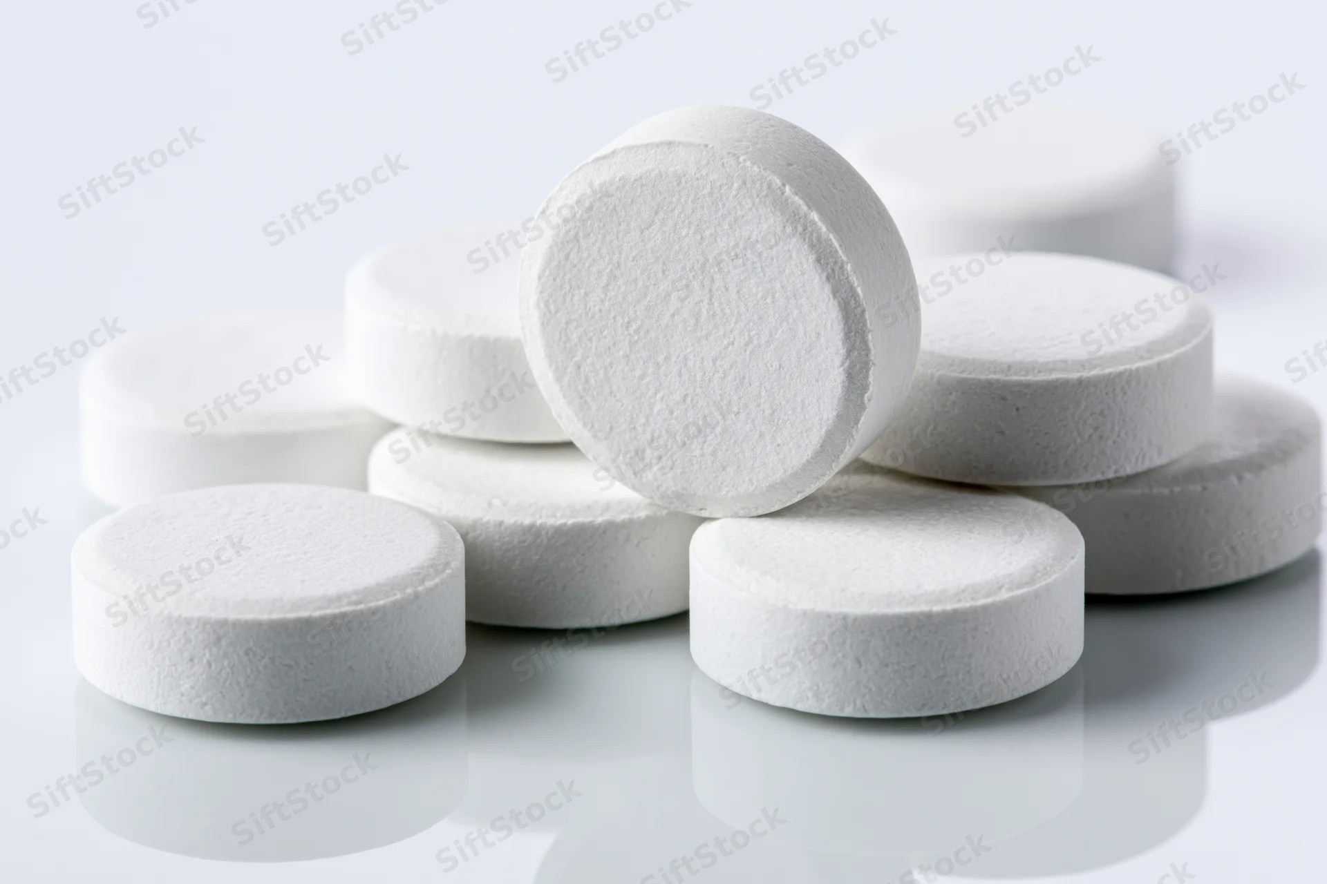 Round white pharmaceutical tablets scattered on a reflective white surface